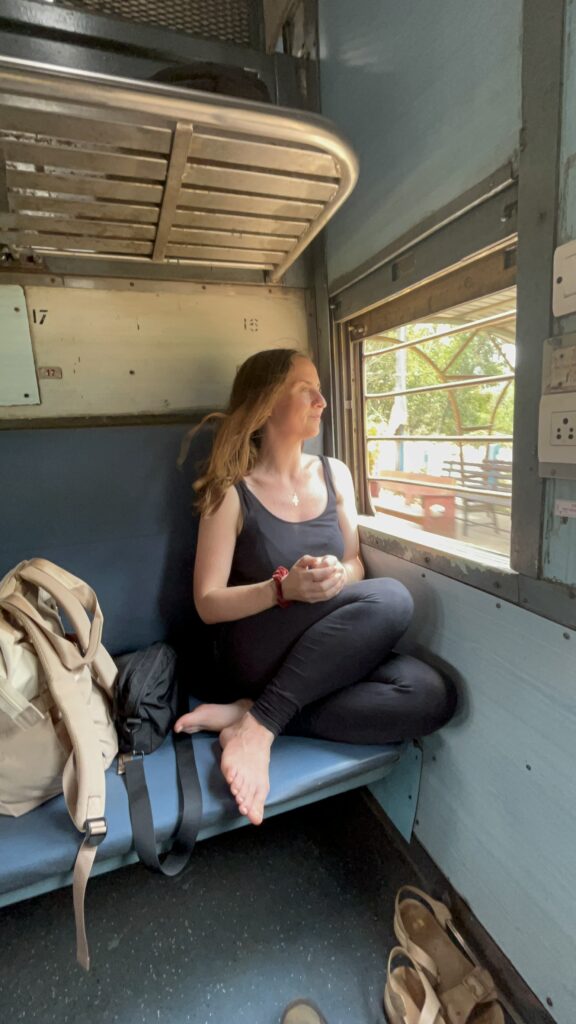 Sally, founder of Lush Lunar, looking out of a train window in India, reflecting on spirituality, energy healing, and Eastern philosophy, inspired by Indian culture and history