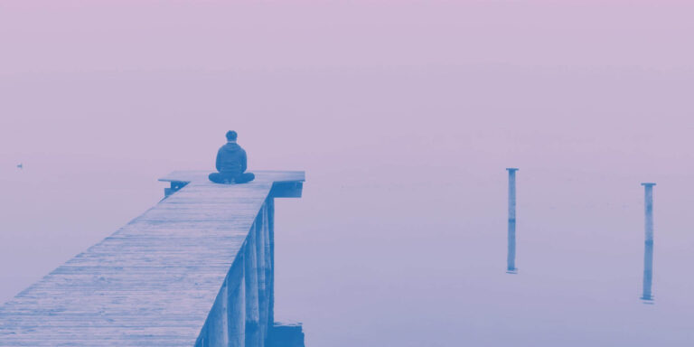 Person meditating at the end of a pier overlooking a calm lake, symbolizing spiritual healing, transformation, and inner reflection.